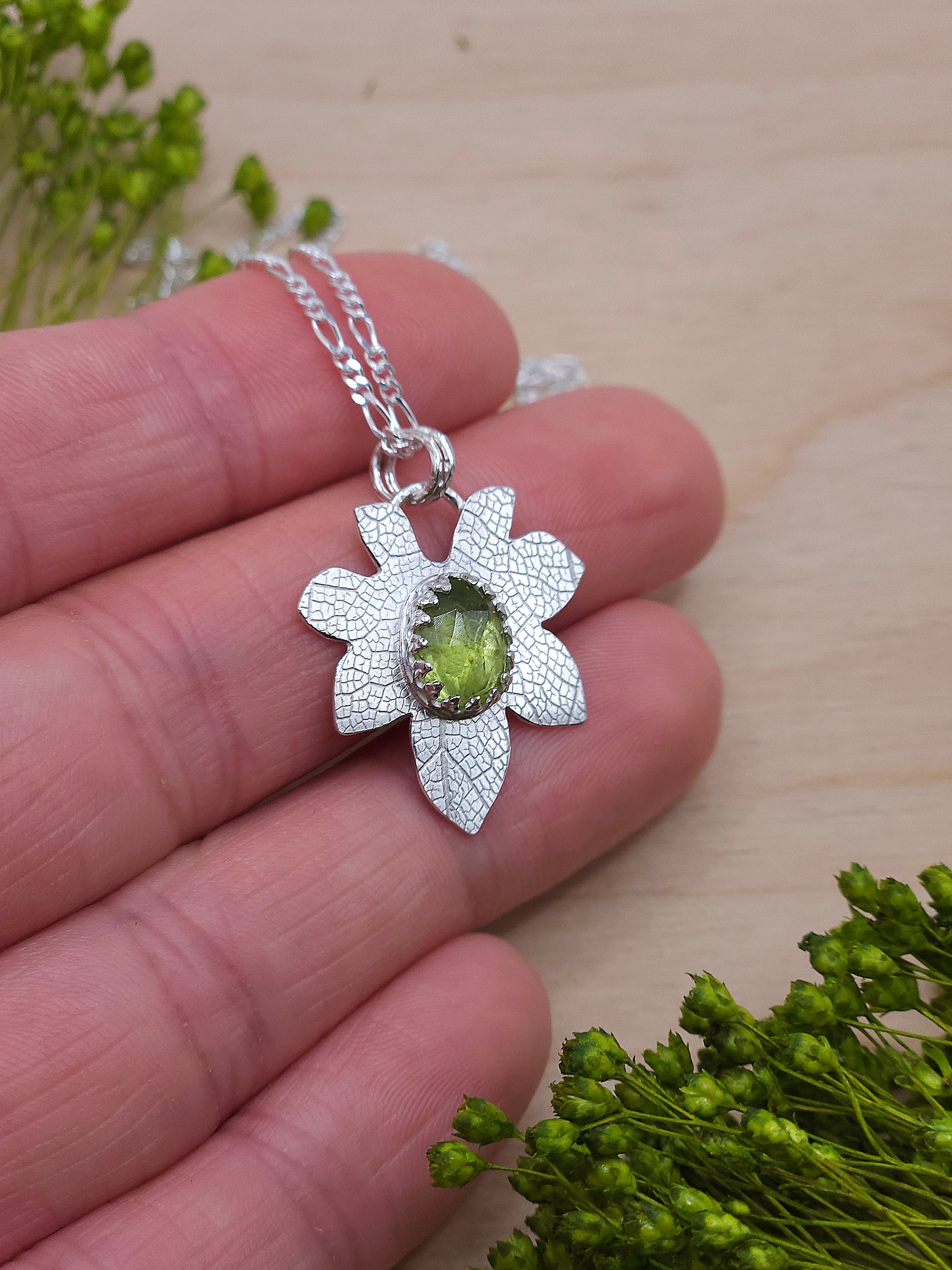 A hand showing off the silver Peridot leaf pendant.