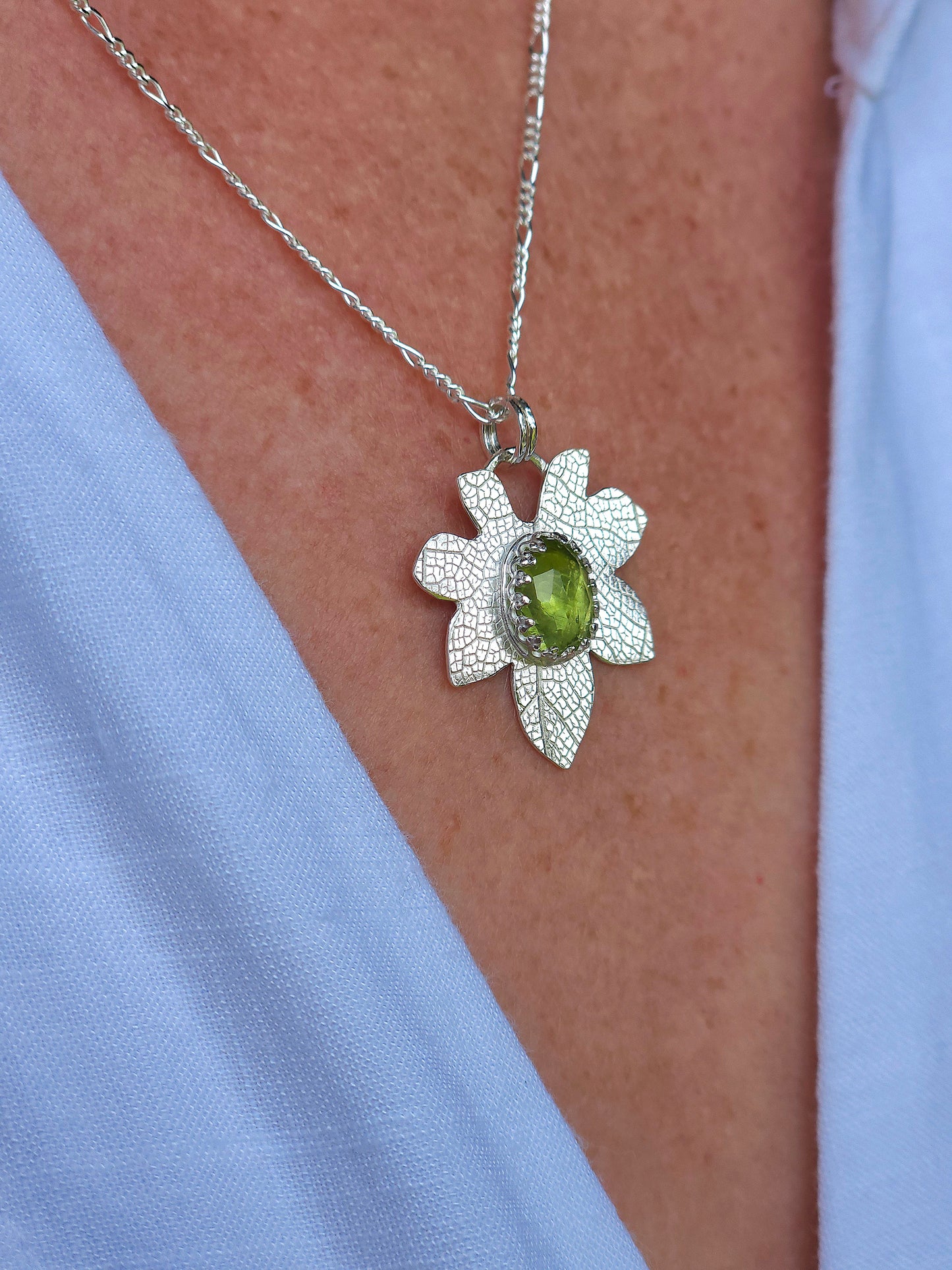 A close up of the Peridot leaf pendant being worn with a white shirt.