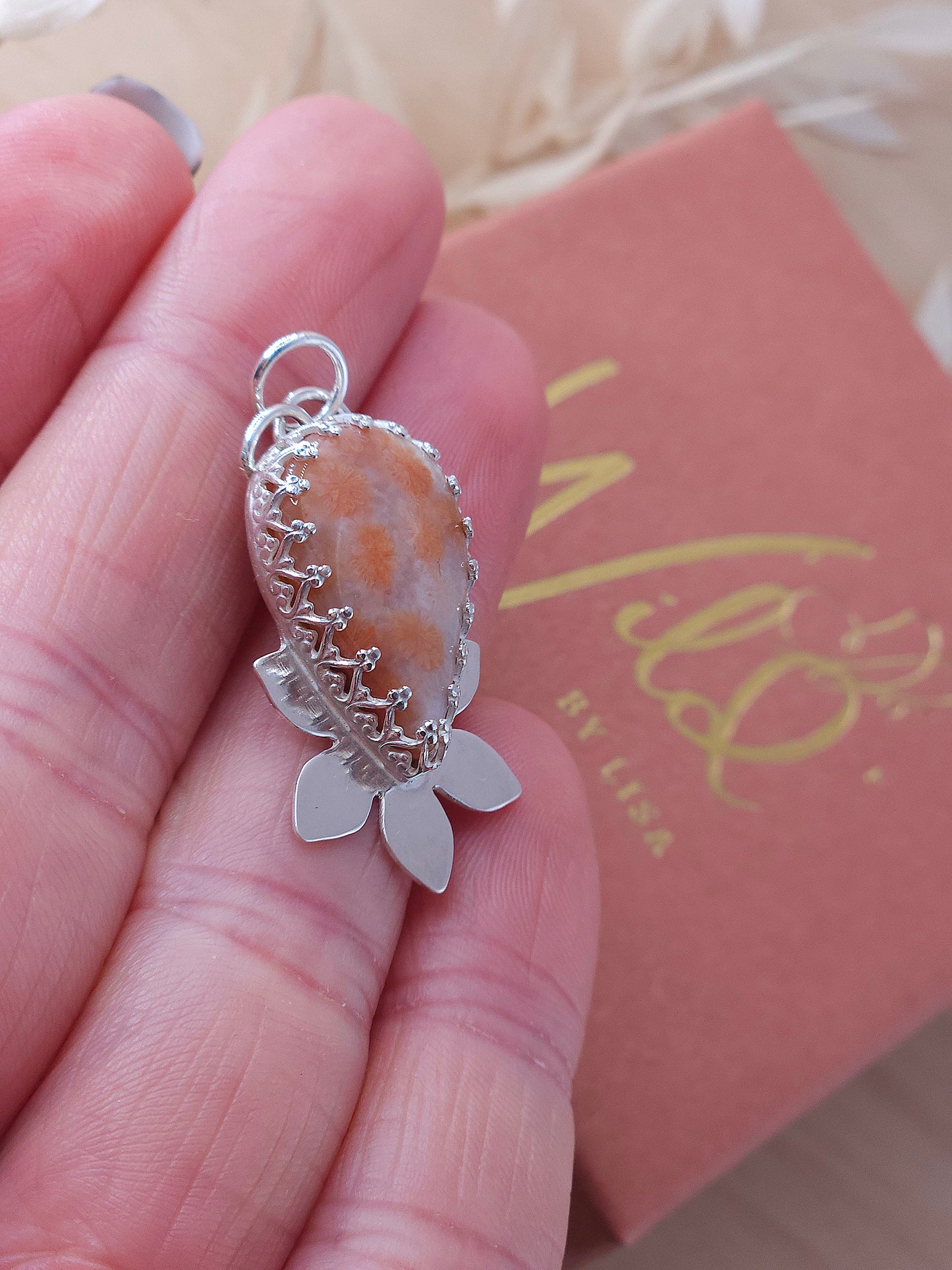 A side view of the peachy pink fossil coral flower necklace showing the fancy pattern bezel wire surrounding the gemstone.