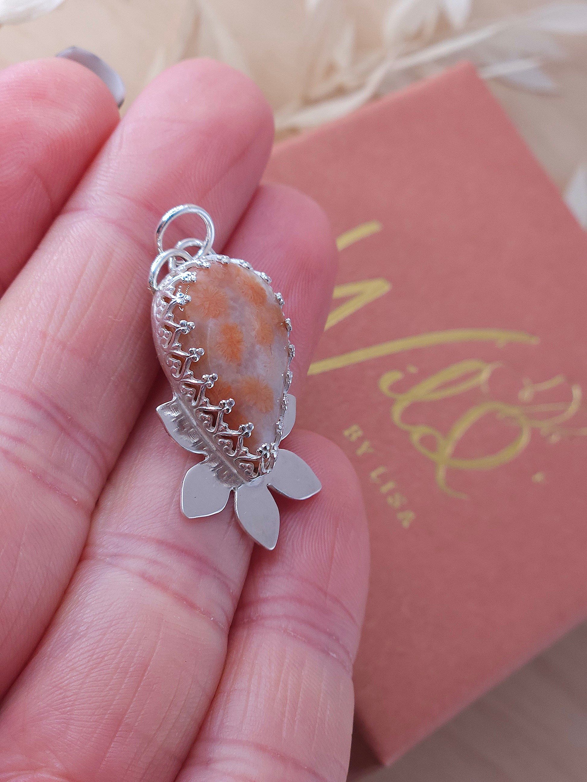 A side view of the peachy pink fossil coral flower necklace showing the fancy pattern bezel wire surrounding the gemstone.