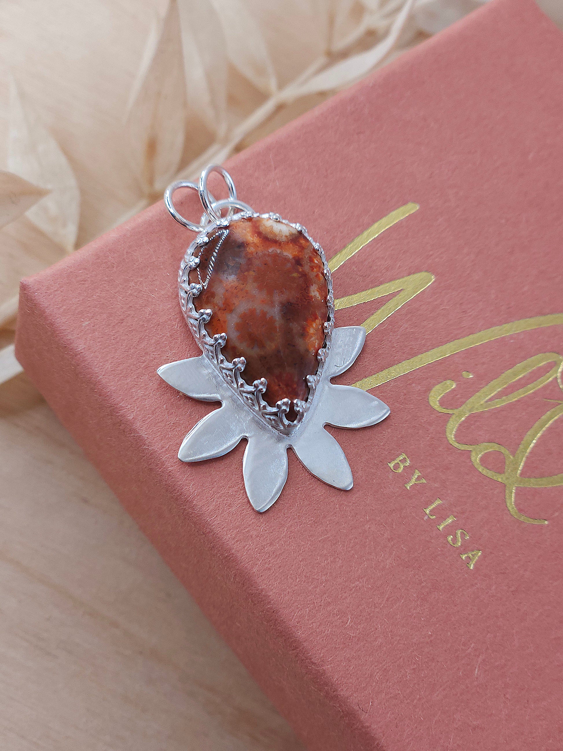 A sterling silver flower necklace featuring a natural red fossilised coral gemstone.