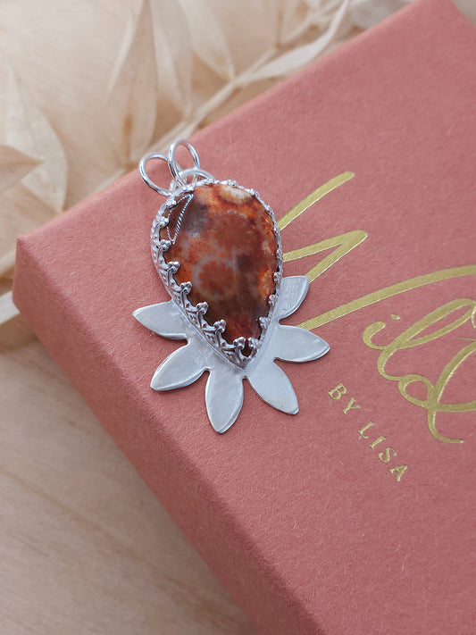 A sterling silver flower necklace featuring a natural red fossilised coral gemstone.