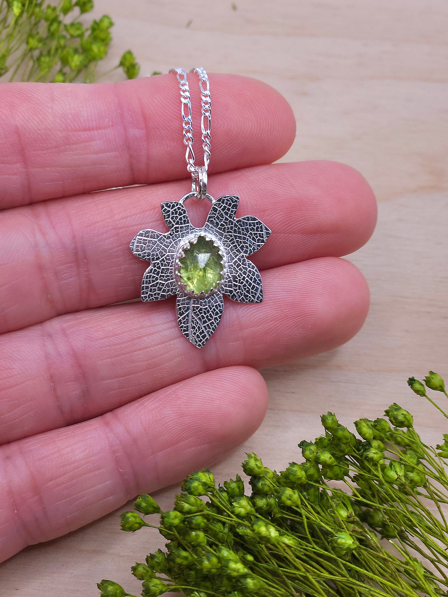 A hand showing off the silver leaf pendant featuring a natural Peridot gemstone.