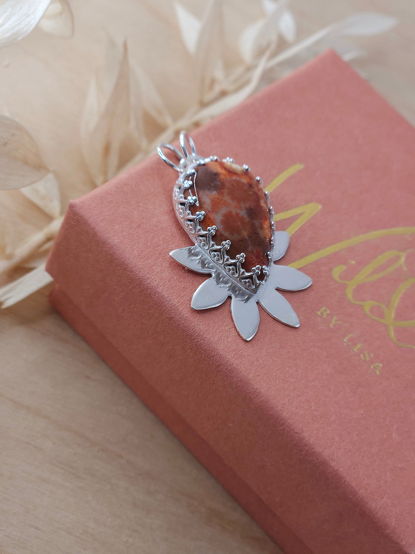A side view of the red fossil coral flower necklace showing the fancy patterned bezel wire surrounding the gemstone.