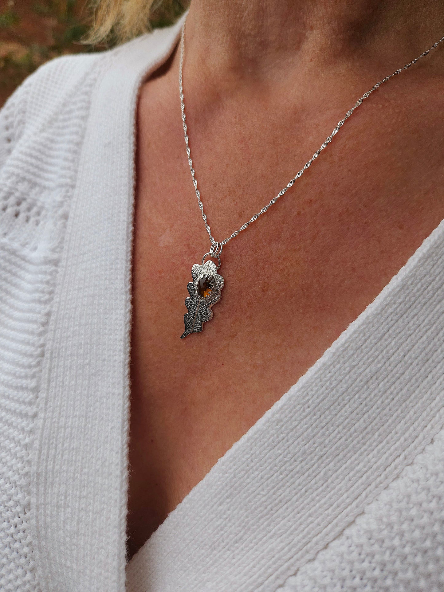 The brown tourmaline leaf necklace being worn with a white cardigan. It hangs on an 18 inch twisted curb chain.