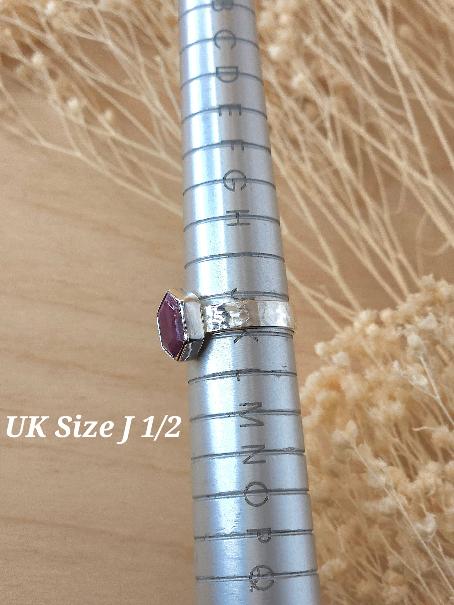 A jewellers ring mandrel holding a silver gemstone ring which sits at UK size J 1/2.