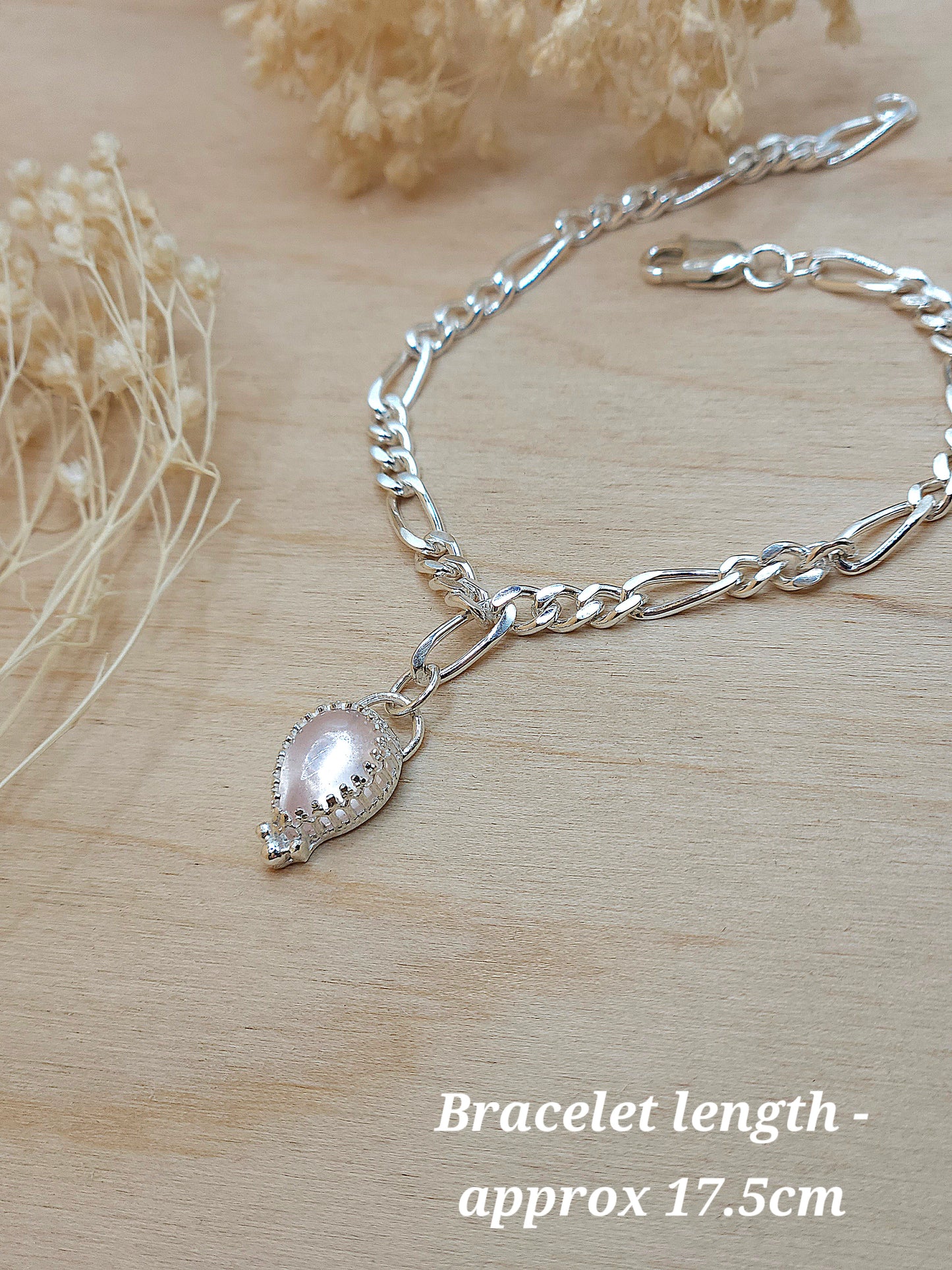 A rose quartz gemstone silver chain bracelet laying on a wooden background with dried flowers. The words 'Bracelet length - approx 17.5cm) written at the bottom of the photo.