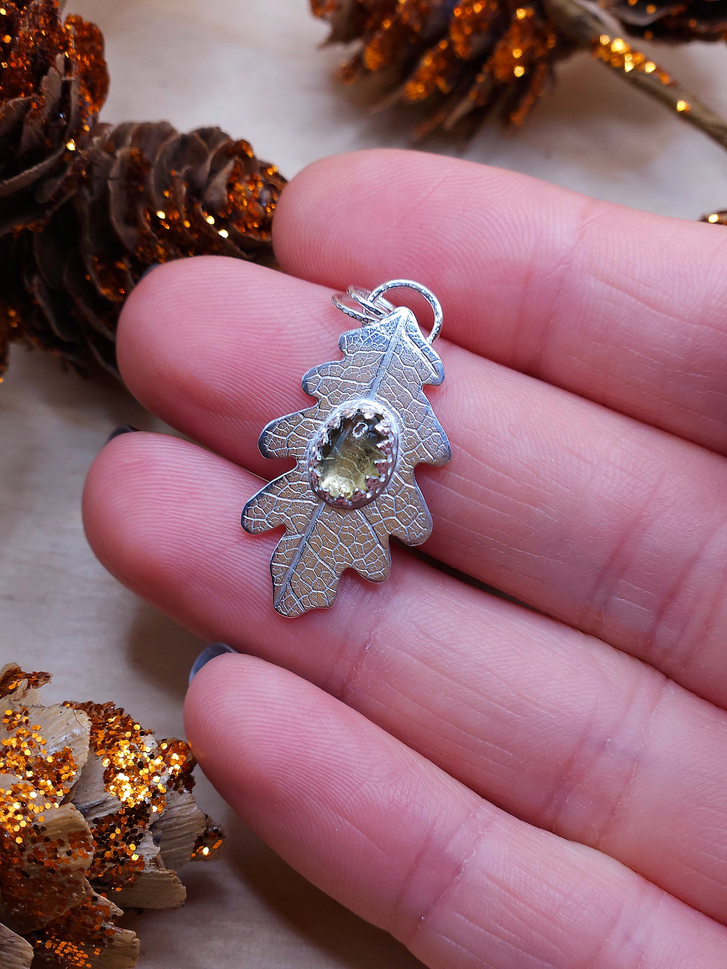 A hand holding the tourmaline leaf pendant.