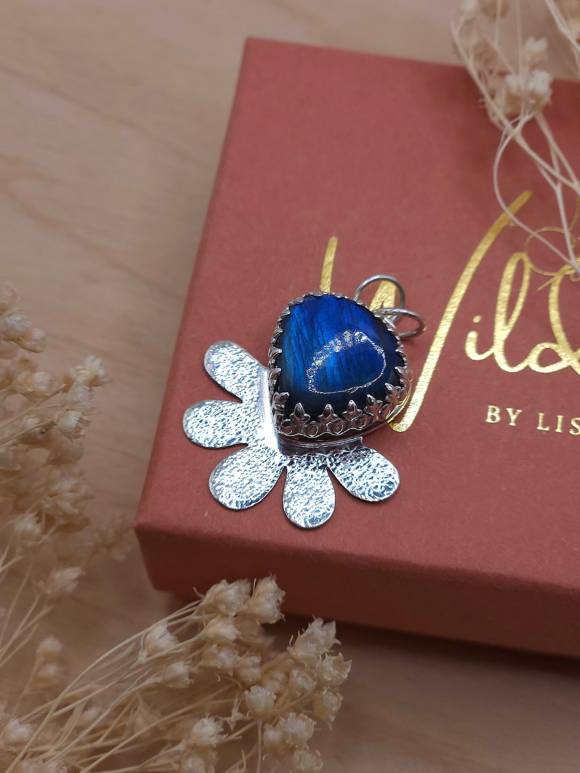 A blue Labradorite hammered silver flower pendant sitting on a Wild by Lisa gift box.