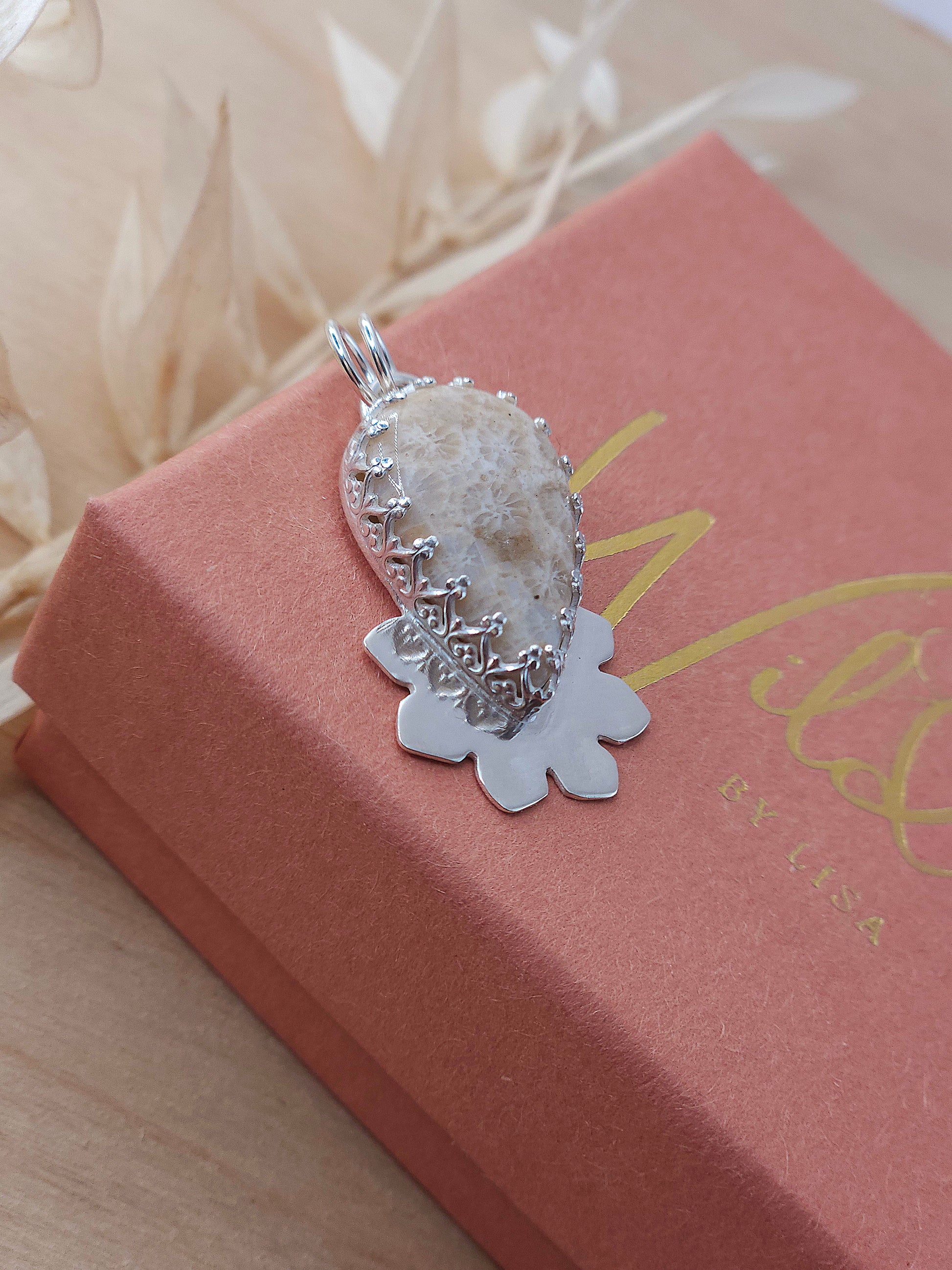 A side view of the beige fossilised coral silver pendant. Showing the fancy pattern bezel wire surrounding the gemstone.