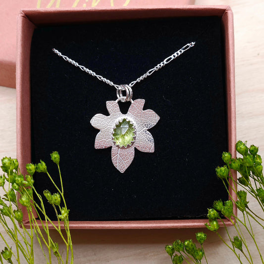A sterling silver leaf necklace featuring a natural Peridot gemstone. Shown in a gift box.