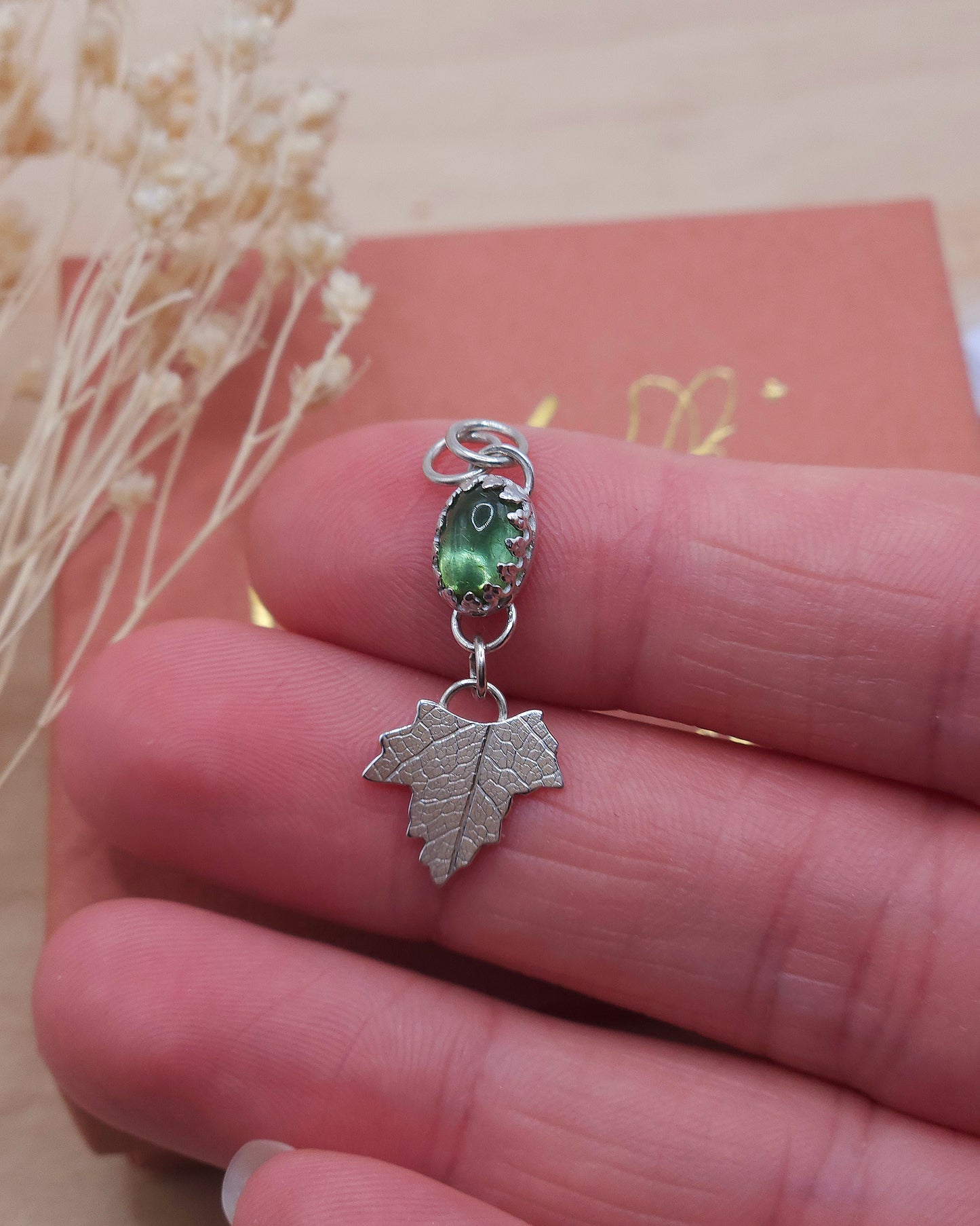 A hand showing off the green tourmaline leaf pendant up close.