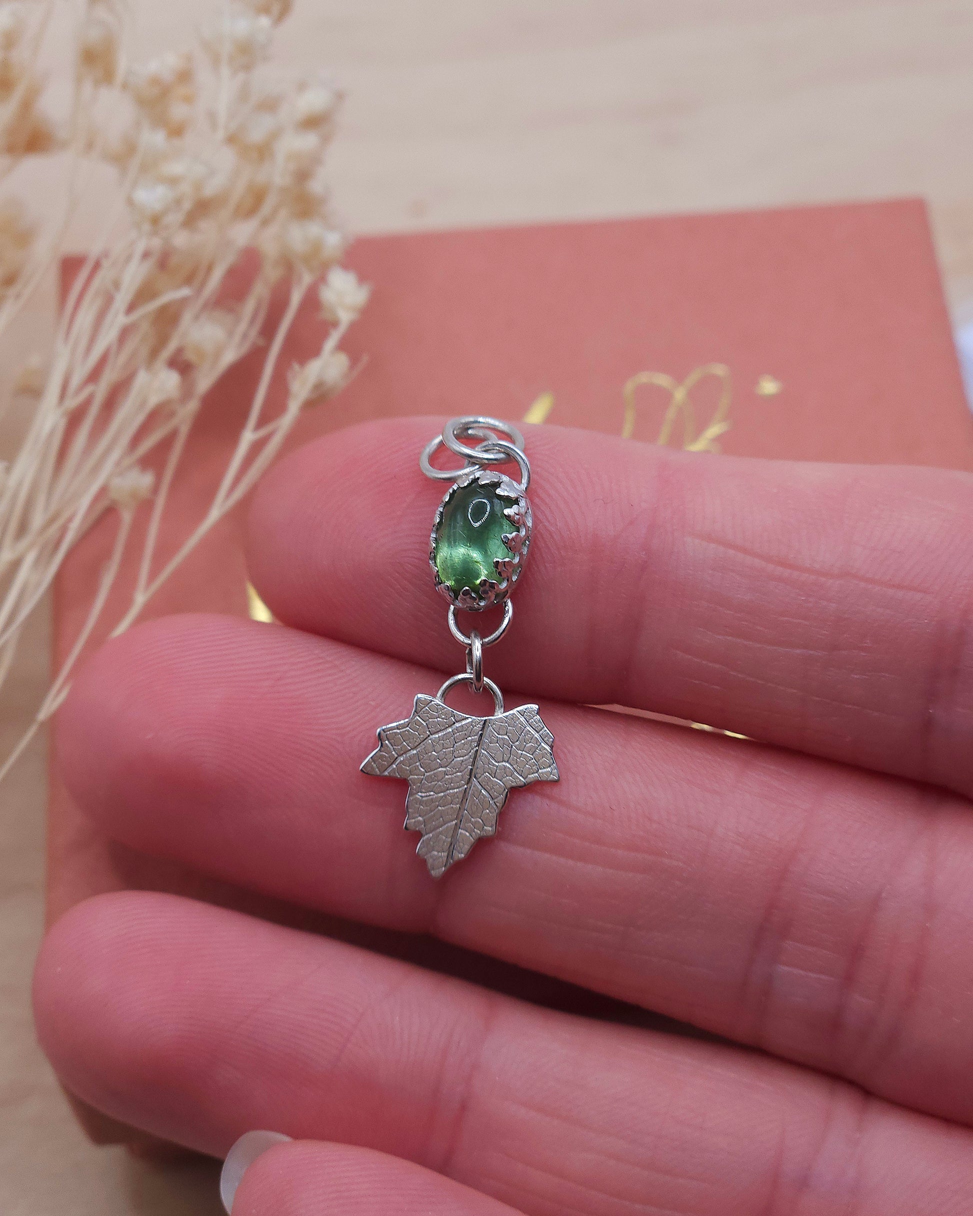 A hand showing off the green tourmaline leaf pendant up close.
