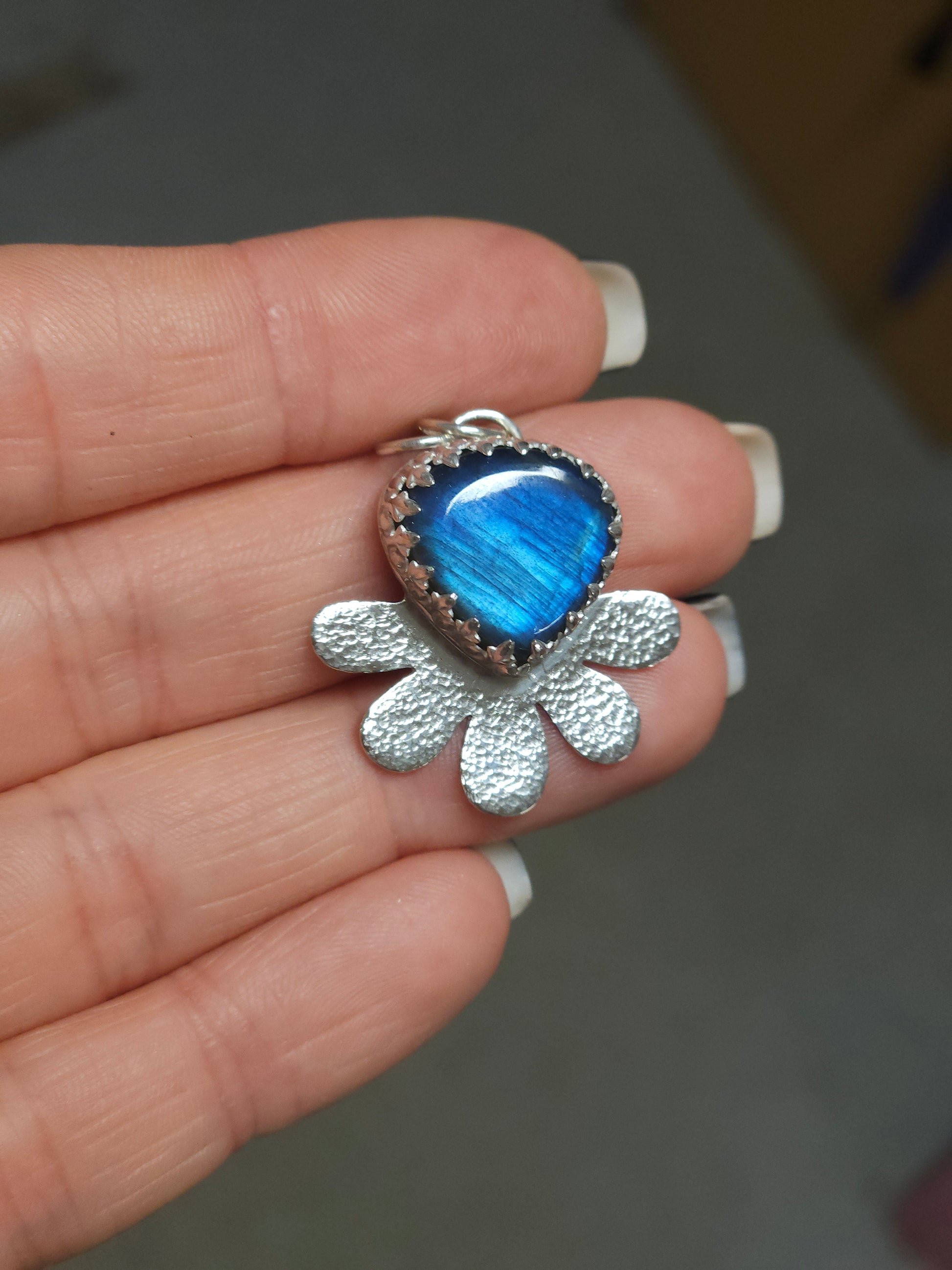 A hand holding the silver hammered flower necklace with Labradorite gemstone.