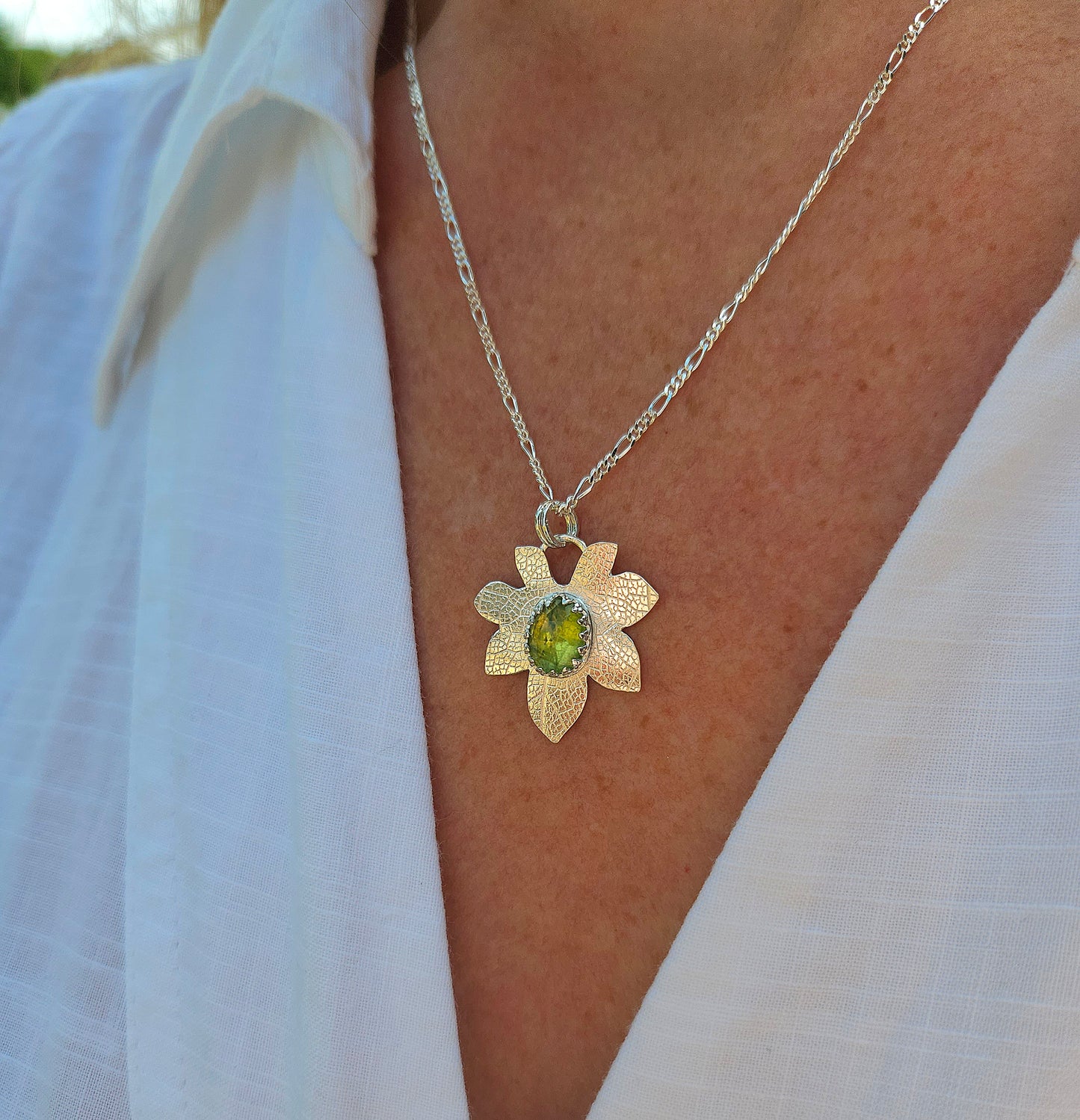 A sterling silver leaf necklace with a Peridot gemstone. Worn with a white shirt.