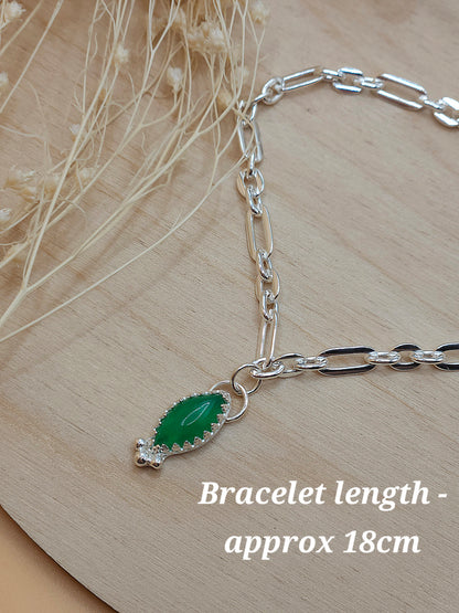A silver link chain bracelet with aventurine charm displayed on a wooden background with dried flowers. Wording on the bottom right of the photo reads - 'Bracelet length - approx 18cm'.