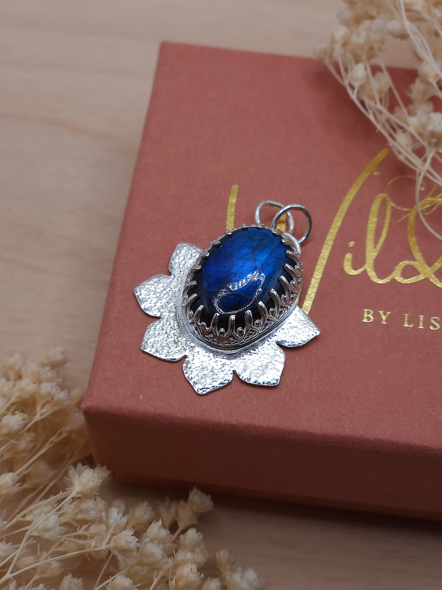 A sterling silver flower pendant with a hammered texture featuring a blue Labradorite gemstone. 