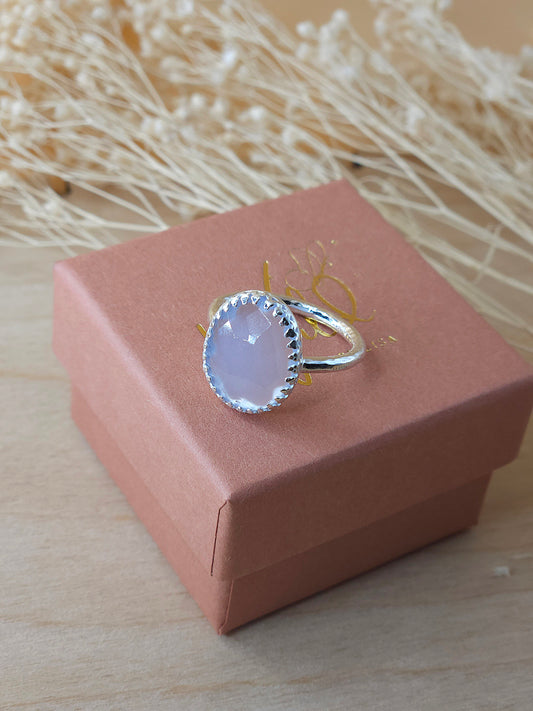 A chalcedony flower ring with a hidden flower detail, displayed on a terracotta gift box. The ring has a lightly hammered band and the gemstone is a lovely translucent lilac colour.