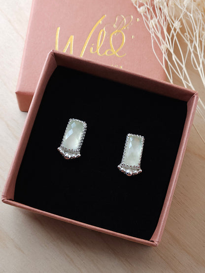 A pair of silver stud earrings with green prehnite gemstones and silver embellishments. Display on a black foam insert inside an open gift box.