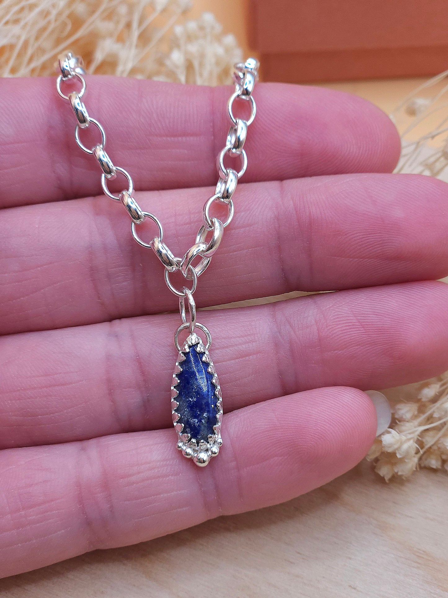 A hand holding a sterling silver charm bracelet with a navy blue coloured Lapis Lazuli gemstone