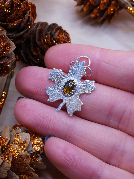 A hand holding a sterling silver leaf pendant with a brown tourmaline gemstone.