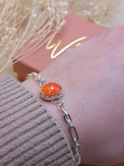 A silver chain bracelet with orange carnelian gemstone worn on a wrist.
