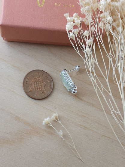 A single silver earring with a green prehnite gemstone laying on it's side next to a one pence coin to show the size comparison.
