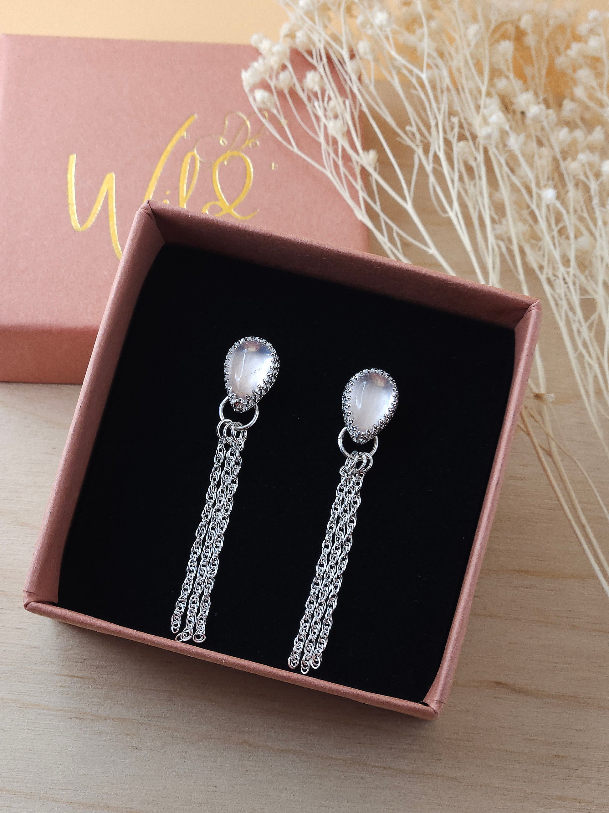 A pair of silver chain dangle earrings with rose quartz gemstones displayed in an open gift box on a black foam insert.