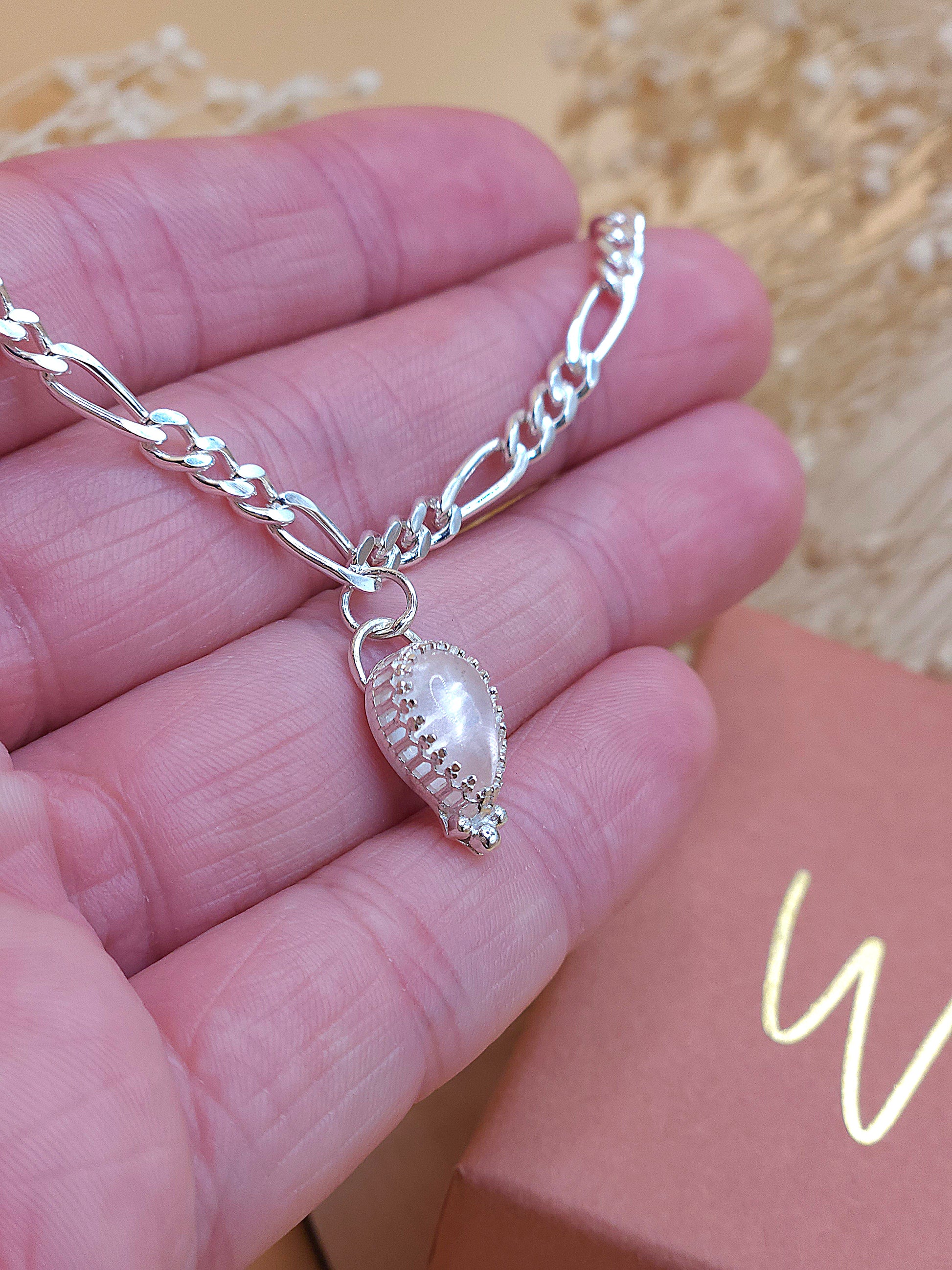 A hand holding a silver chain bracelet with rose quartz gemstone, showing the side of the gemstone bezel setting.
