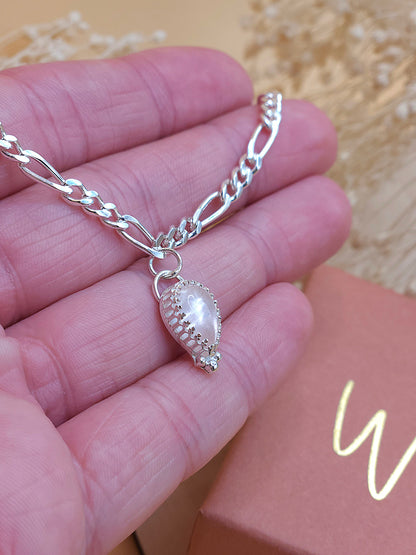 A hand holding a silver chain bracelet with rose quartz gemstone, showing the side of the gemstone bezel setting.