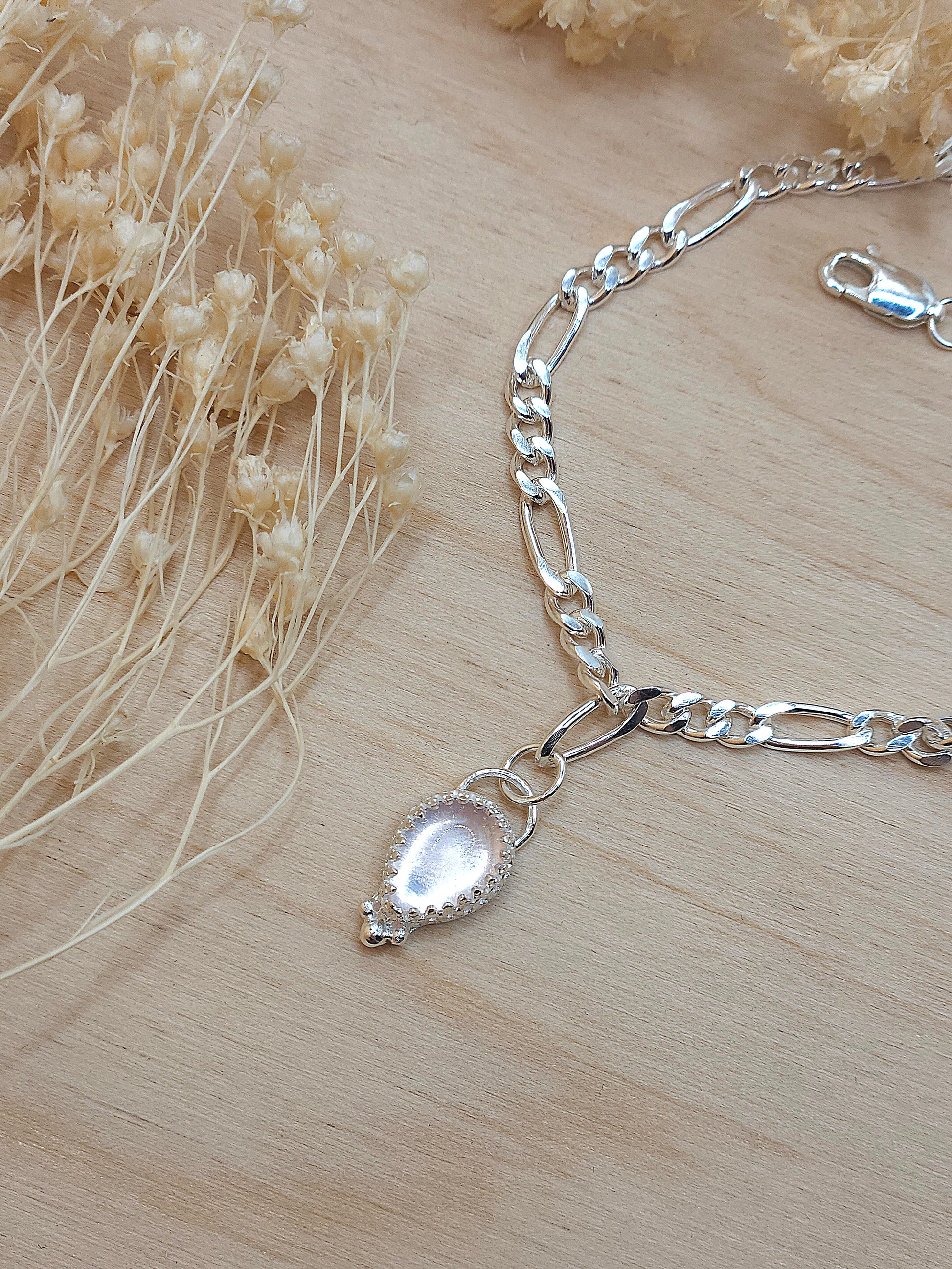 A sterling silver chain bracelet with rose quartz gemstone displayed on a wooden background with dried flowers surrounding it.