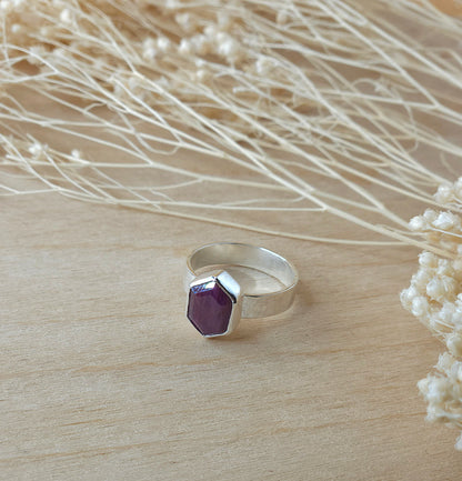 A sterling silver hammered ring with hexagonal natural ruby gemstone, displayed on wooden background with dried flowers.