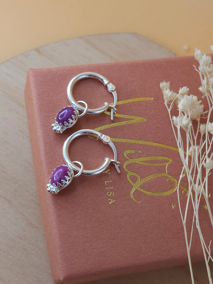 A pair of silver hoop earrings with ruby gemstones lay on a terracotta and gold coloured gift box
