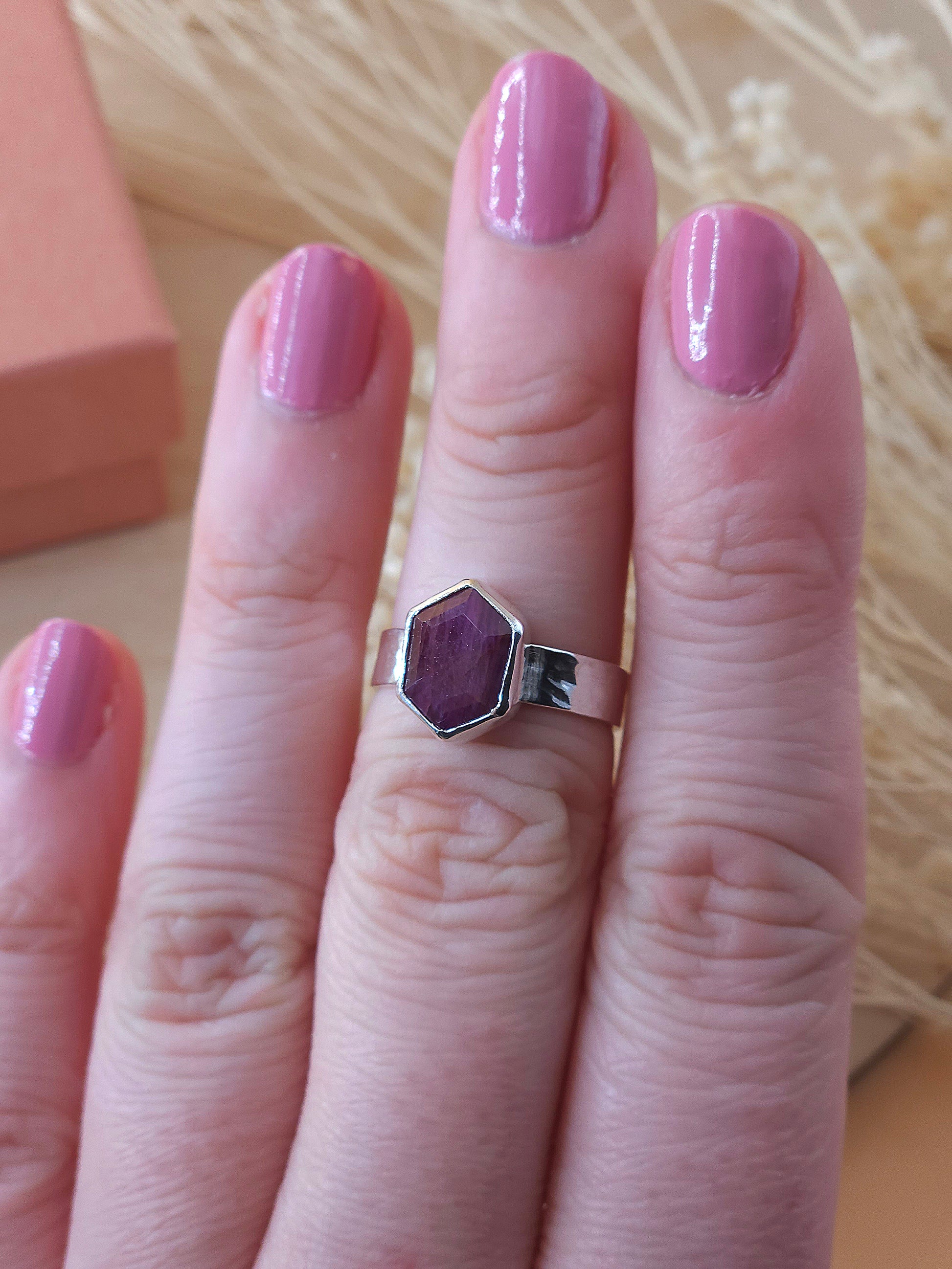 A sterling silver pinkie ring with ruby gemstone displayed on a finger.