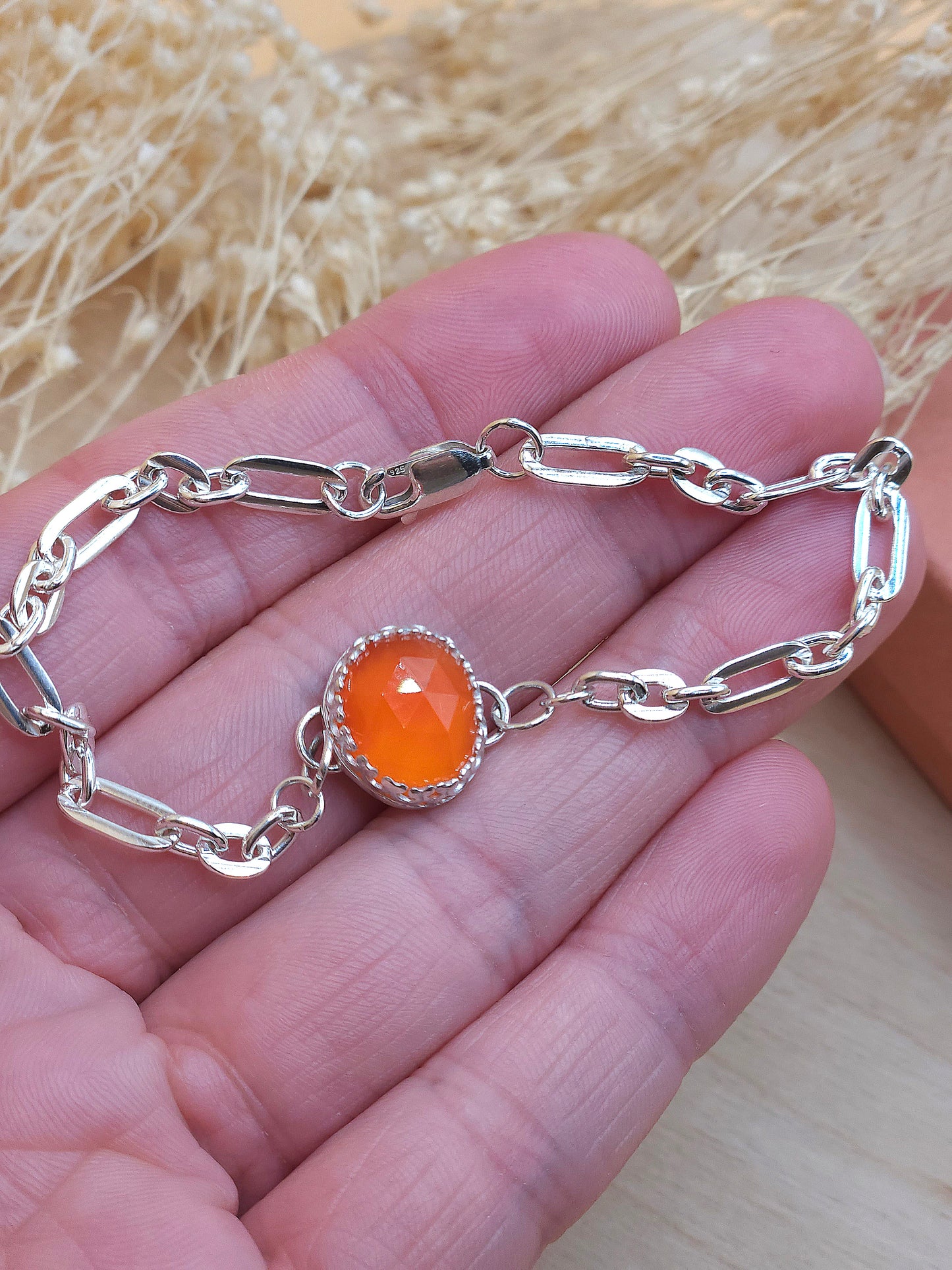 A hand holding the silver link chain bracelet with orange carnelian gemstone.