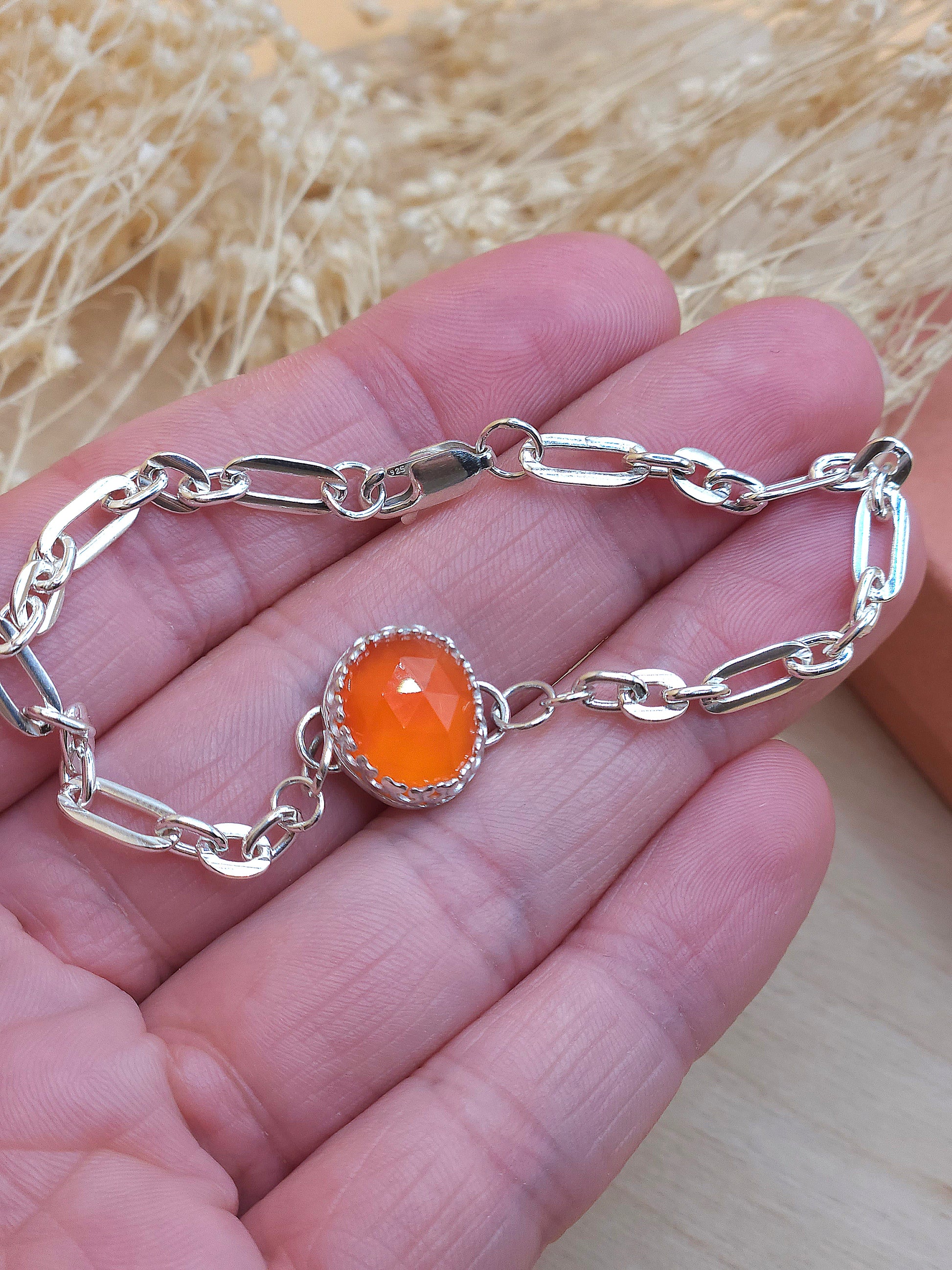 A hand holding the silver link chain bracelet with orange carnelian gemstone.
