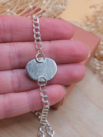 A hand holding a sterling silver chain bracelet, showing the back of the gemstone setting.