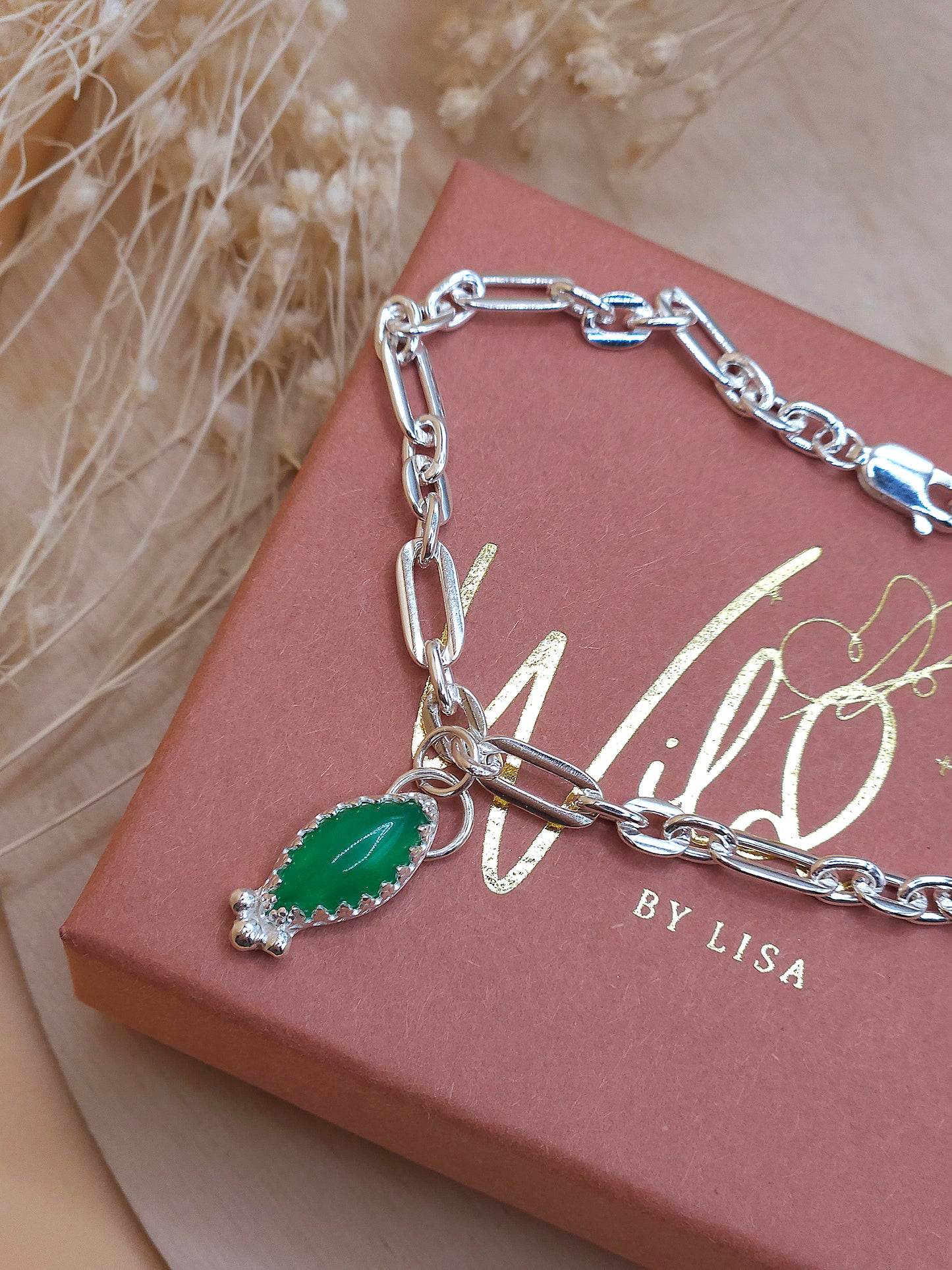 A sterling silver link chain bracelet with green aventurine charm displayed on a terracotta coloured gift box with brand name 'Wild by Lisa' in gold writing.