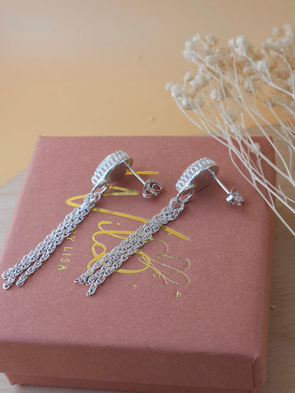 A pair of silver chain dangle earrings lay on a gift box showing the side of the earrings with dried flowers in the background.