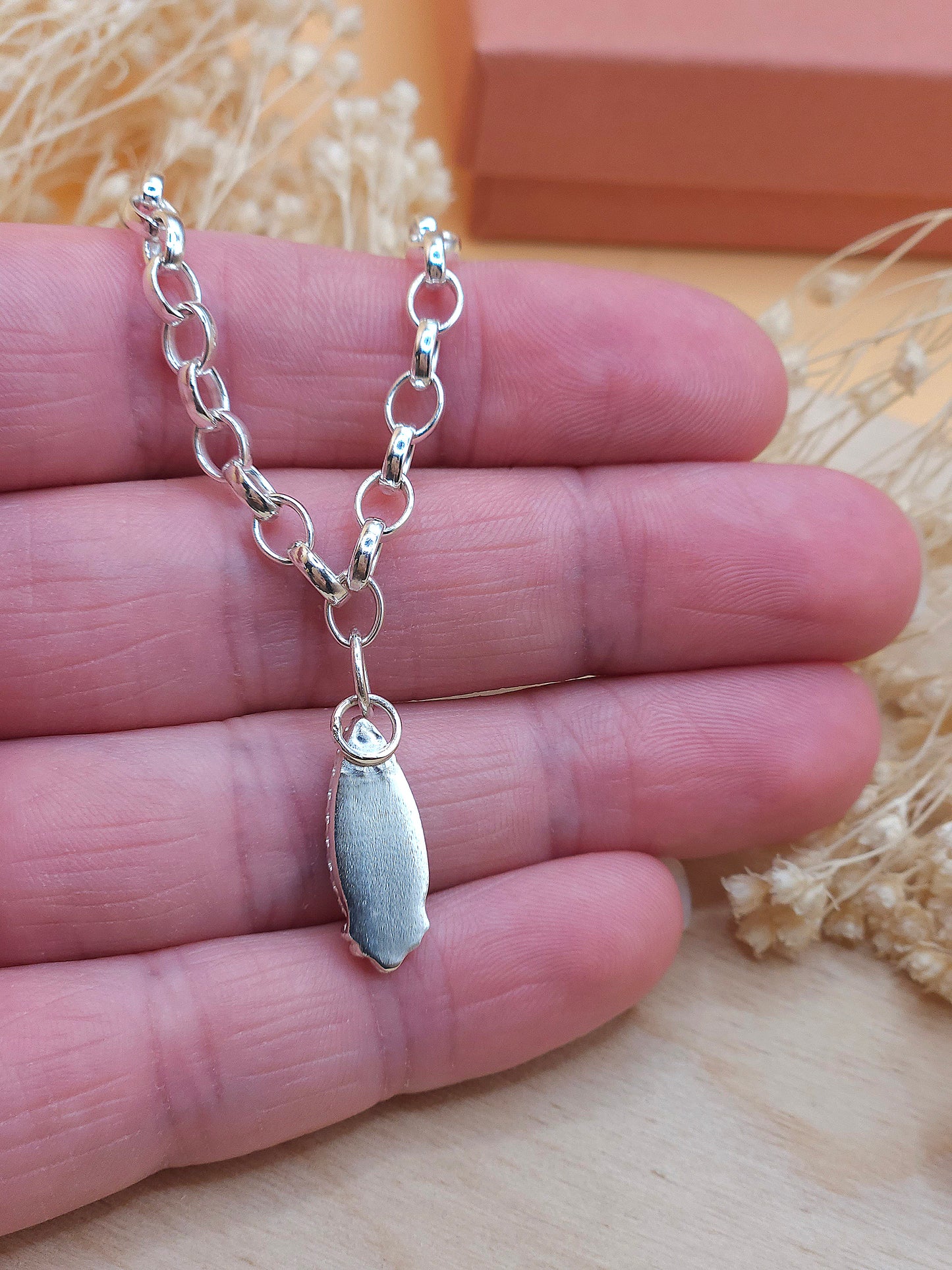 A hand holding a sterling silver chain bracelet, showing the back of the gemstone setting.