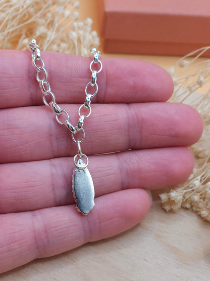 A hand holding a sterling silver chain bracelet, showing the back of the gemstone setting.