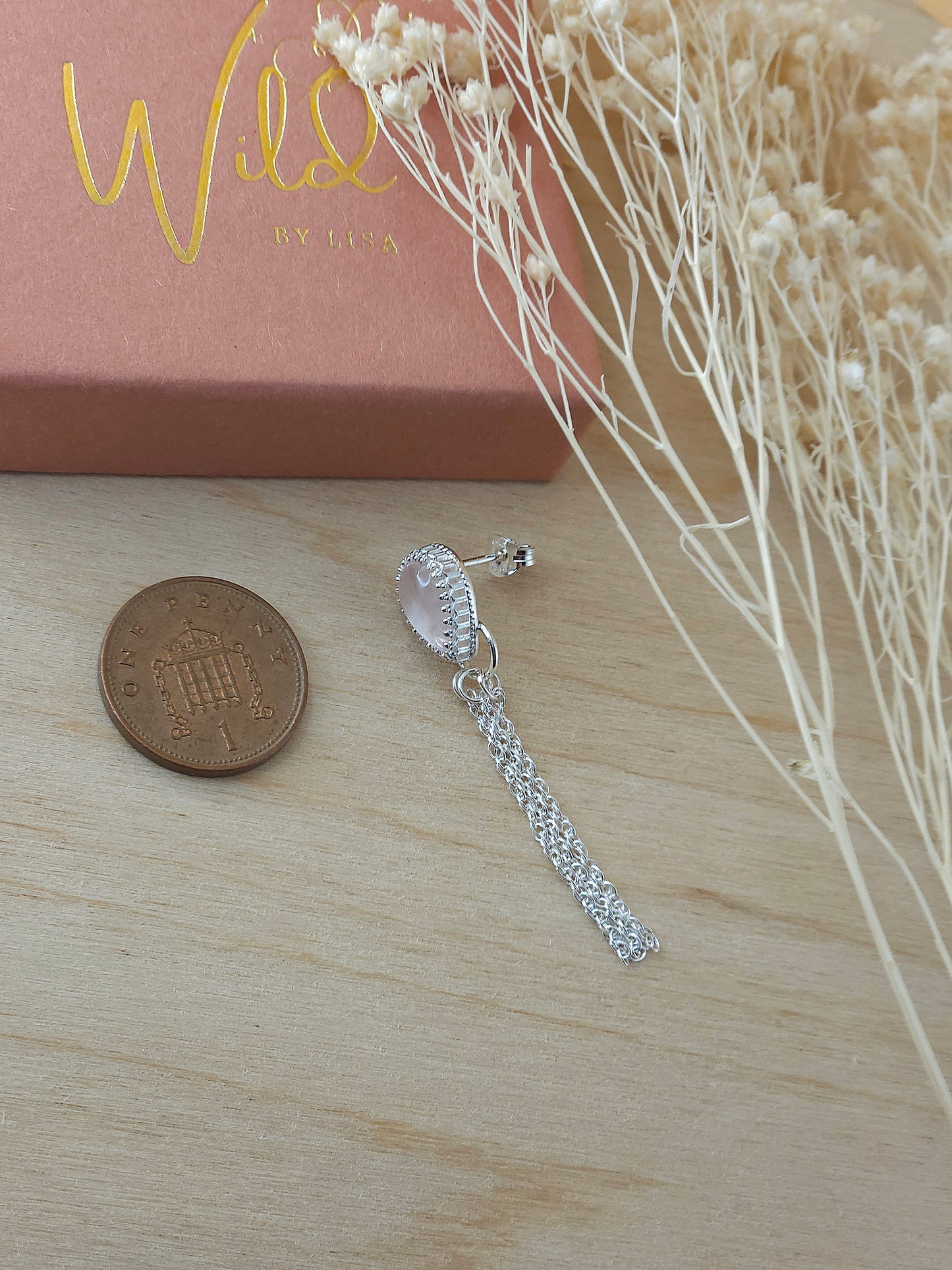 A single silver earring with rose quartz gemstone lay next to a one pence coin to show the size.