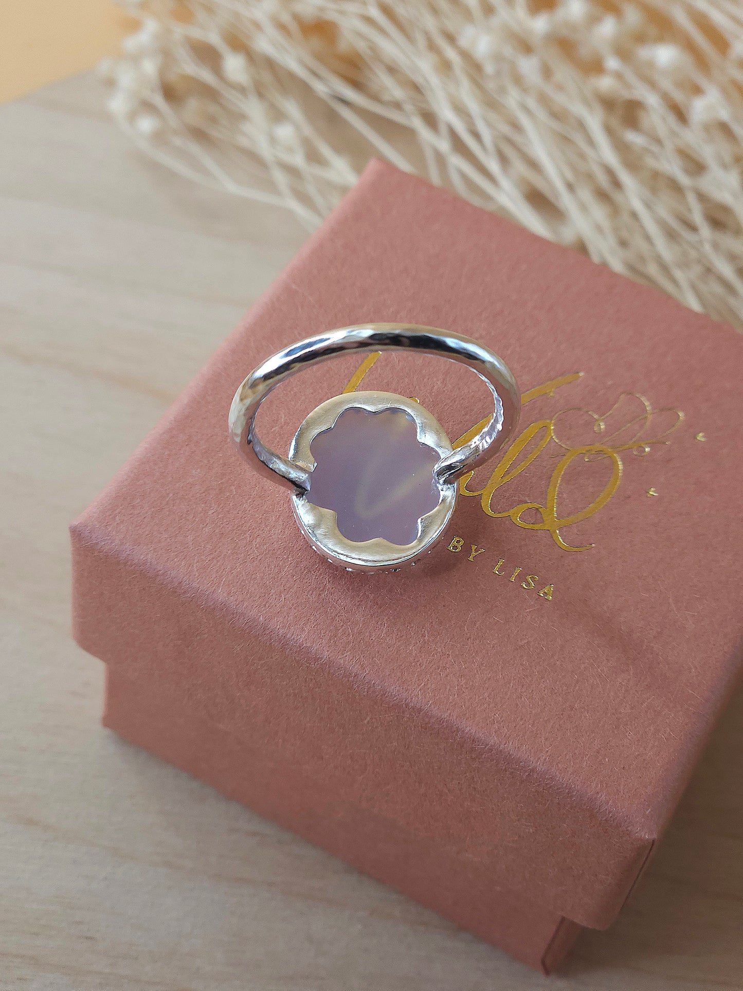 A sterling silver ring with hammered band displayed on a gift box showing the hidden flower detail on the back of the gemstone setting.