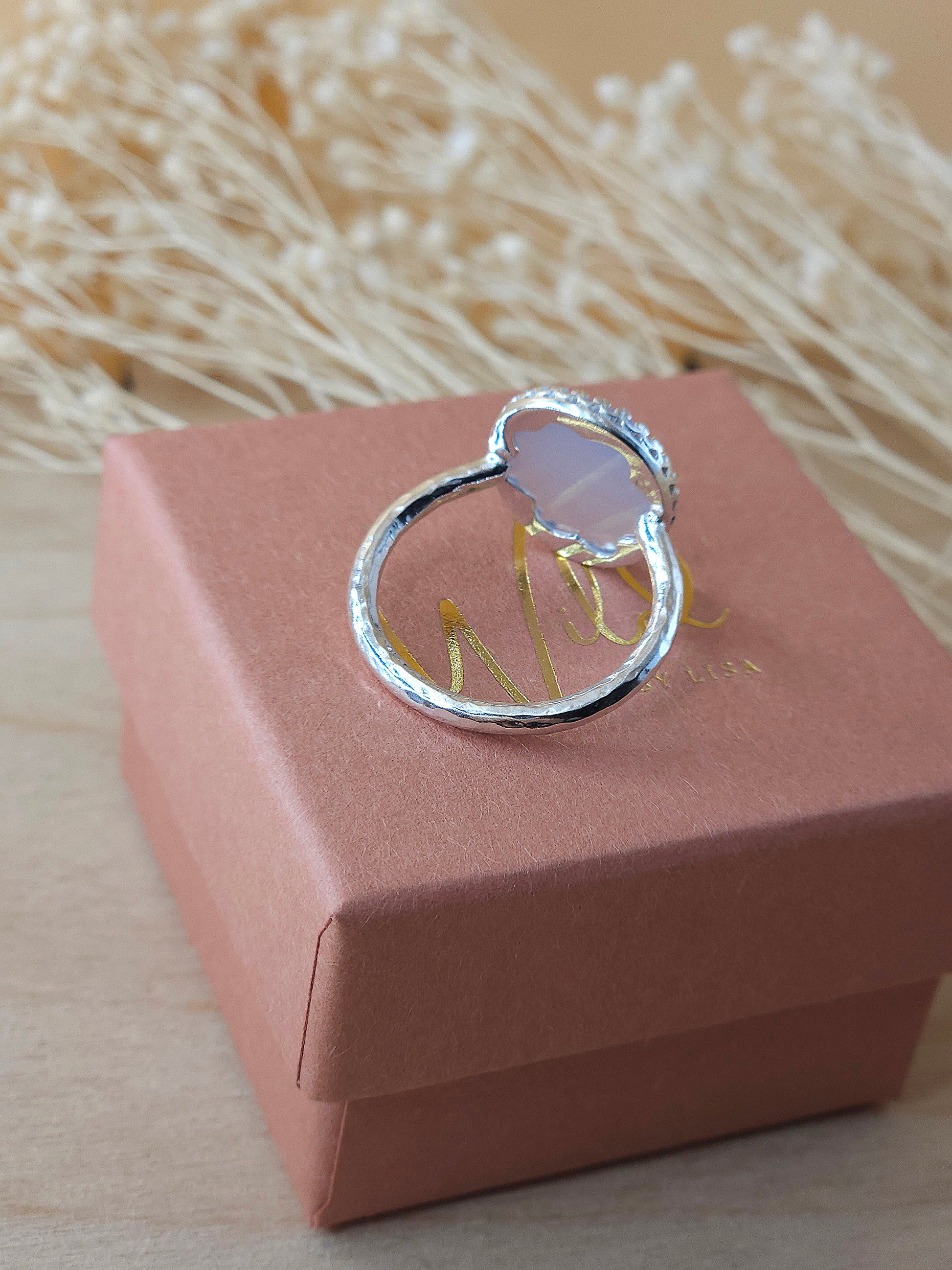 A sterling silver gemstone ring displayed on gift box with dried flowers in the background, showing the back of the gemstone setting.