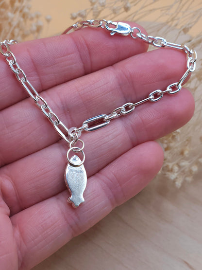 A hand holding a sterling silver link chain bracelet, showing the back of the gemstone setting.