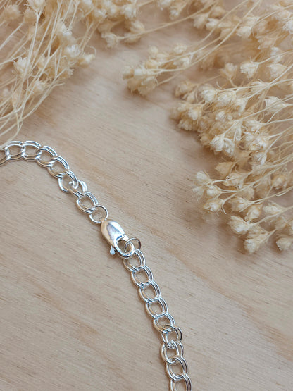 A sterling silver chain bracelet displayed on a wooden background with dried flowers, showing the lobster clasp.