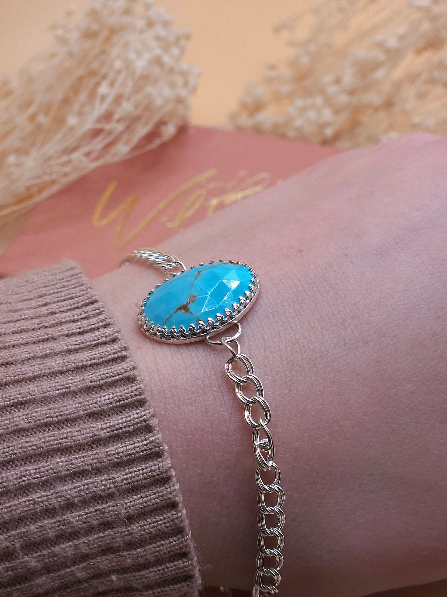 A turquoise chain bracelet worn on a wrist with dried flowers in the background.