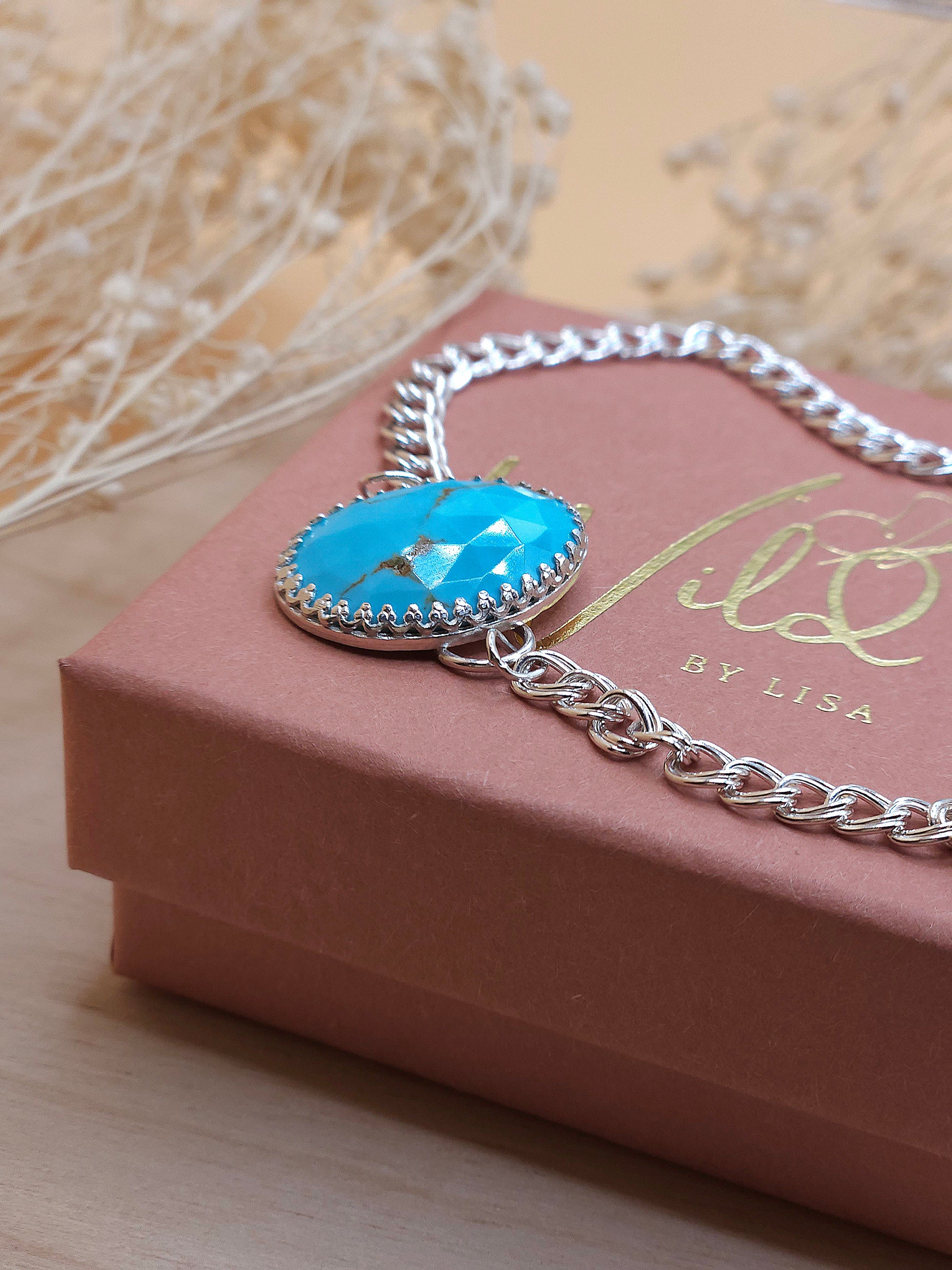 A sterling silver chain bracelet with a blue turquoise gemstone, displayed on a gift box showing the side view of the gemstone setting.
