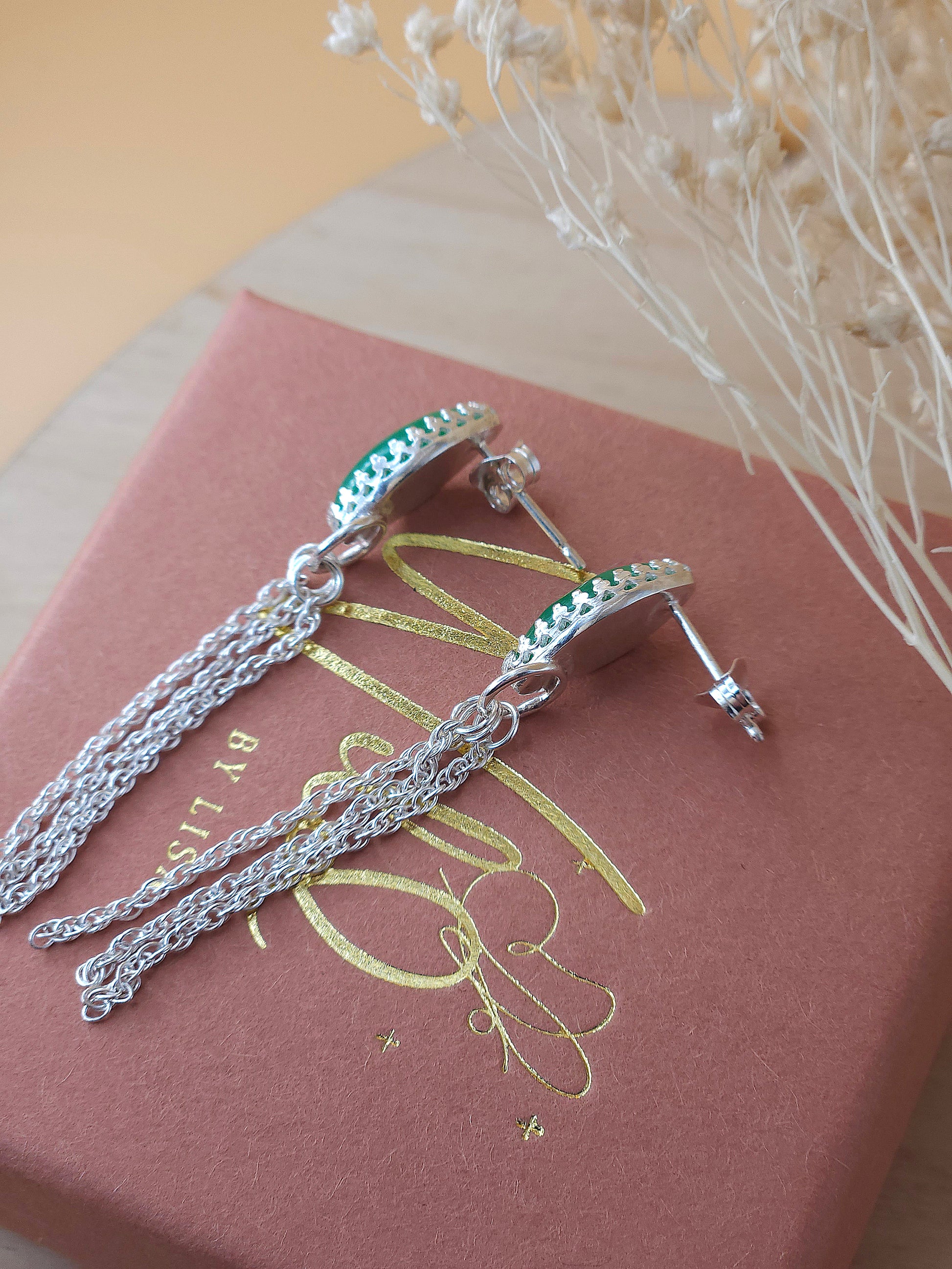 A pair of silver chain dangle earrings lay on a gift box showing the side view.