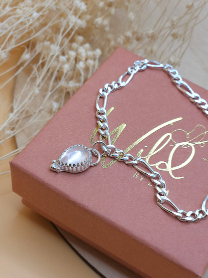 A silver chain bracelet with a rose quartz gemstone charm displayed on  a gift box with dried flowers in the background.